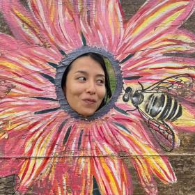 Grace in a flower head cutout looking at a painted bee.