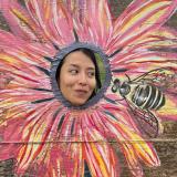 Grace in a flower head cutout looking at a painted bee.